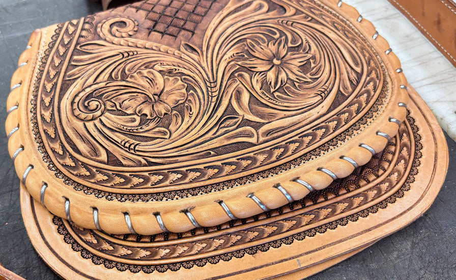 Brown leather bag with intricate embossed design on a dark surface